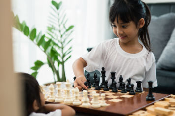 Asian girl playing chess with white and black pieces on wooden board