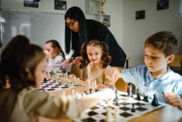 Chess students competing against one another while chess teacher stands over top of them